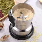 Stainless steel grinder with ground ingredients on a light surface