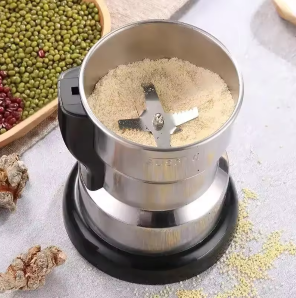 Stainless steel grinder with ground ingredients on a light surface