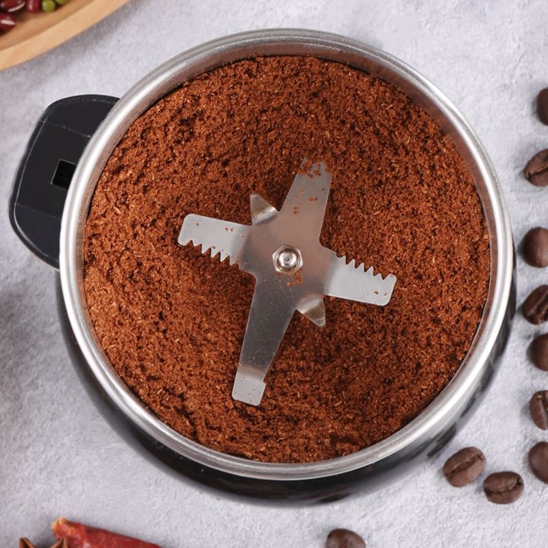 Coffee grinder with ground coffee and coffee beans on a gray surface